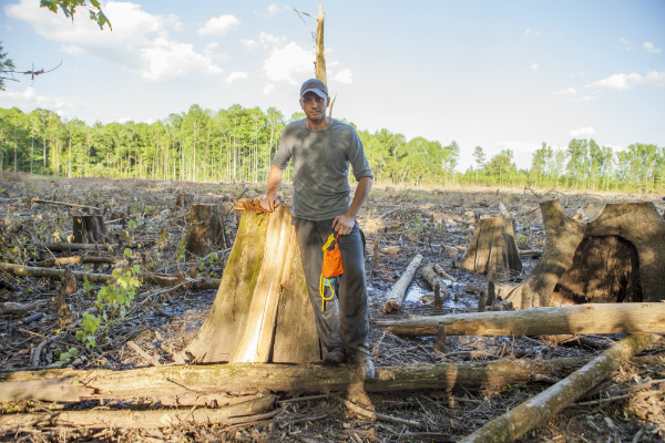 Adam Colette standing next to a large cypress stump in front of a wetland clearcut