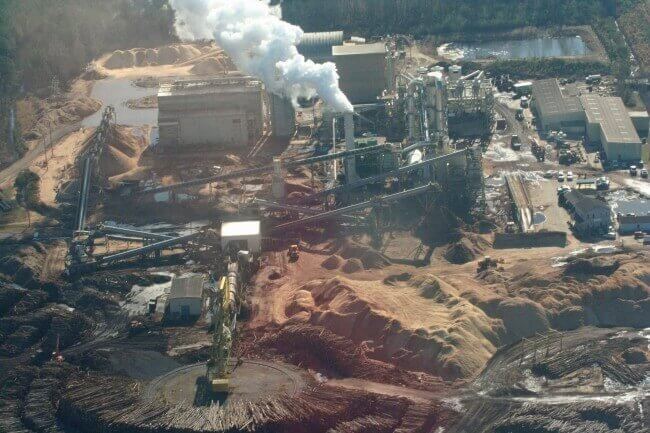 Overhead view of Enviva's facility in Ahoskie North Carolina. Large industrial plant with steam emissions from towers, dirt piles and construction, and huge piles of timber logs